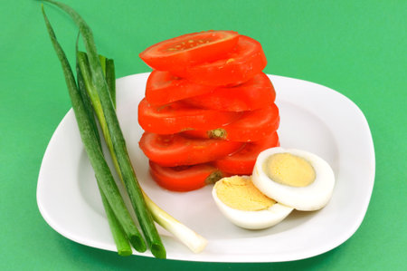 Tomato beautifully cut with egg and onion rests on a white plateの写真素材
