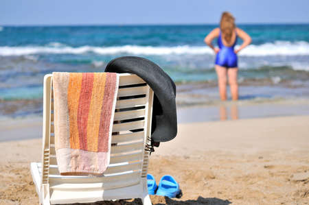 
	
A hat, a towel hanging on a chair on the beach by the sea, and in the distance a woman の写真素材