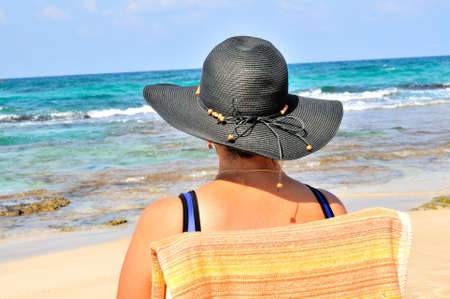 
	
A woman sits in a chair on the beach by the seaの写真素材
