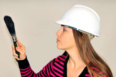 A girl in a white helmet, holding a paintbrush against the wallの写真素材