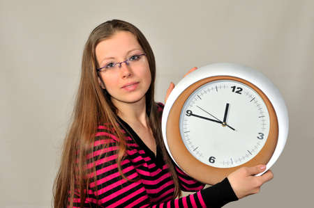 A young girl holding a wall clock against a gray backgroundの写真素材