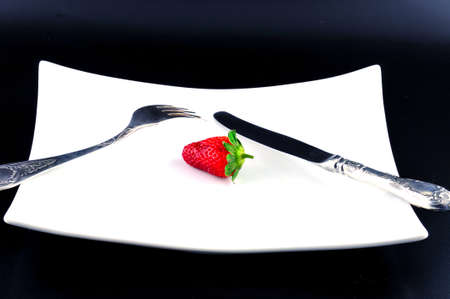 Knife and fork are on a white plate next to a strawberryの写真素材