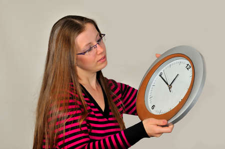 A young girl holding a wall clock against a gray backgroundの写真素材