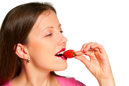 Beautiful girl takes a bite out a piece of strawberry keeps her leavesの写真素材