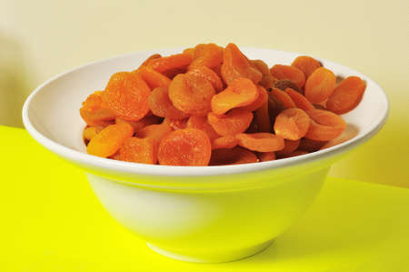 Dried apricots are in a deep white plate against a yellow backgroundの写真素材