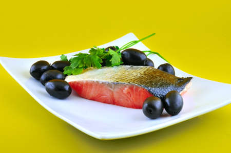 Part of salted fish salmon lying on a white plate beside large black olivesの写真素材