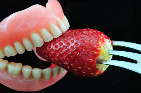 Strawberries sandwiched  artificial teeth, photographed against a black background