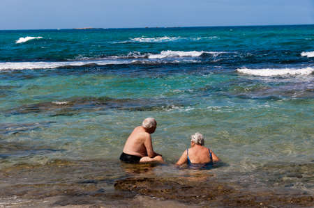 A pair of elderly pensioners came on a hot day to sit and cool off in the sea waterの写真素材
