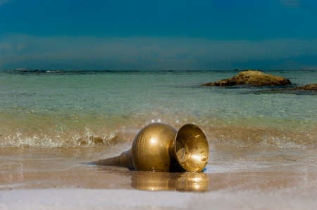 Bronze vintage lamp lying on the sand in the sea water near the coastの写真素材