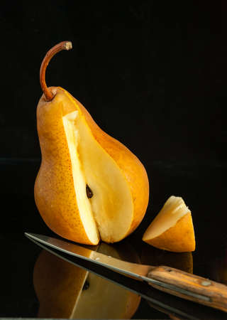 Pear, a knife and a cut  slice  on a black background with reflectionの写真素材
