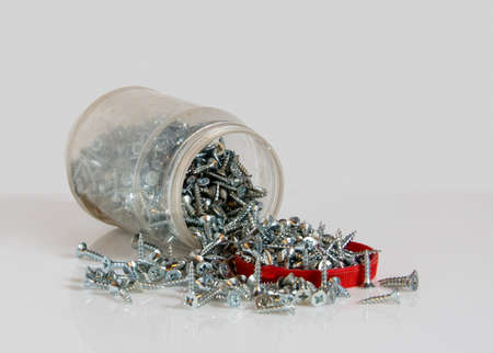Transparent can with a red lid and scattered screws. Photo on the white backgroundの写真素材