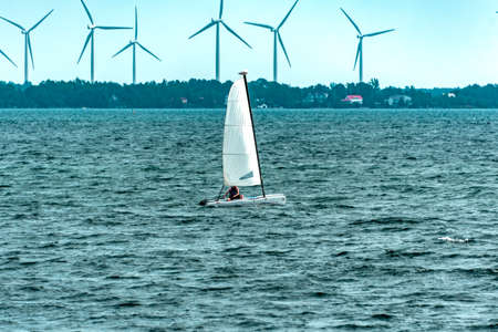 the catamaran sails past the island on which the wind turbines are installedの写真素材