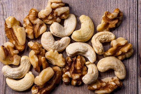 Raw cashews and walnut kernels lie, mixed in a bunch, on a wooden table