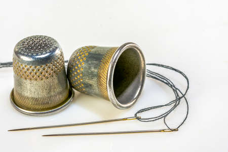 Two sewing needles with black thread and two sewing thimbles lie on a white backgroundの写真素材