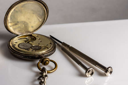 Antiques, vintage swiss pocket watch, two screwdrivers and tweezers lie on a white plastic tableの写真素材