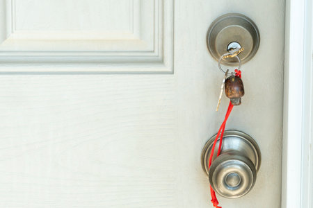 A key with a keychain on a red rope is inserted into the door lock.の写真素材