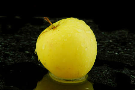 yellow apple on black background with waterの写真素材