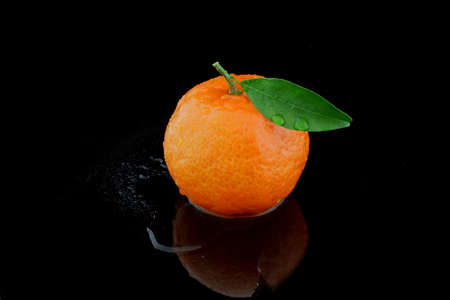 A whole tangerine with leaf on blackの写真素材