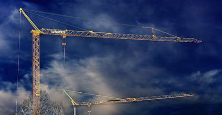 Two construction cranes outdoors under cloudy skyの写真素材