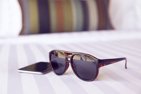 sunglasses and cellphone in the bed room with soft focus.の写真素材