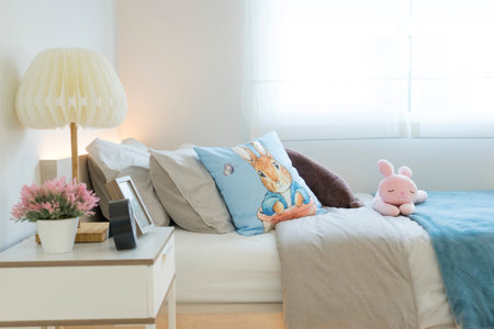 Pink and blue blanket with creative pillows on bed in colorful kids room with white side table and...