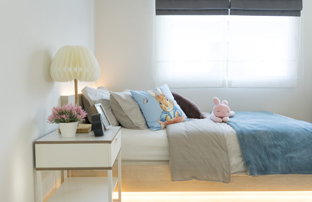 Pink and blue blanket with creative pillows on bed in colorful kids room with white side table and lamp.の写真素材