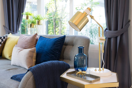 living room interior with yellow , blue and pink pillows on sofa. golden table lamp aside.