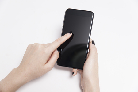 Woman hand holding white mobile phone smartphone on white table background.の写真素材