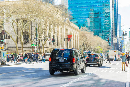 Many cars commute on 5th Ave. with building in the background in New York City, NY