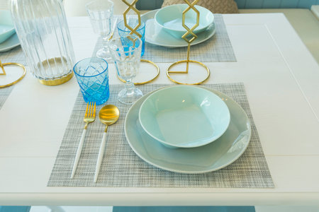 Pale blue plate setting on table with gold candle holder in home dining room interior.