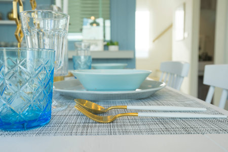 Pale blue plate setting on table with gold candle holder in home dining room interior.