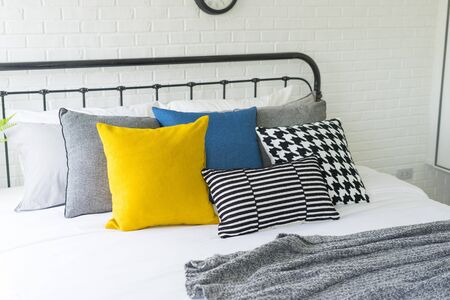 yellow and blue pillows on bed in modern bedroom with many clock on wall.の写真素材