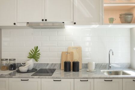 Stylish white kitchen with kitchen island. Green leave in glass vase.の写真素材