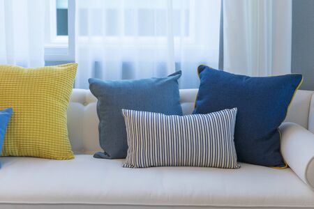 Interior of minimalistic living room with white sofa and yellow, blue cushion.の写真素材