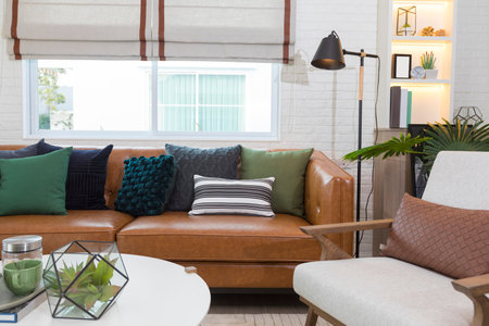 Modern living room with big comfortable leather sofa with green and black pillows on it.