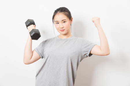 Beautiful young Asian woman lifting dumbbells smiling and energetic isolated over white background. Healthy lifestyle.の写真素材