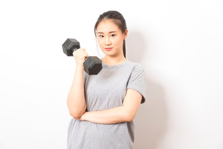 Beautiful young Asian woman lifting dumbbells smiling and energetic isolated over white background. Healthy lifestyle.の写真素材