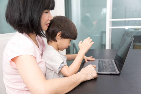 Asian woman with a child works on computer. Concept of work from home and home family education. Mom and son are working on a laptop at home.の写真素材