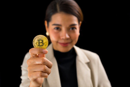 Successful Asian businesswoman standing over black background holding bitcoin money.