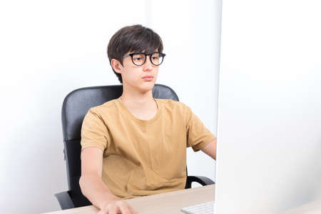 Serious teenage boy sitting on the chair while using computer at home. Online learning with his school classmates during lockdown.の写真素材
