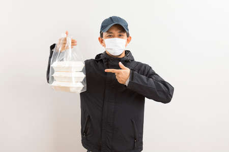 Asian delivery man in protective mask holding food delivery box over white background.の写真素材