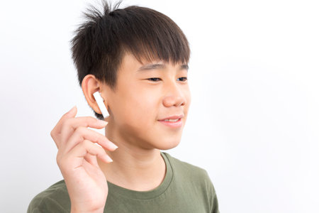 joyful Asian boy 10-12y wearing earpods smiling on white background.