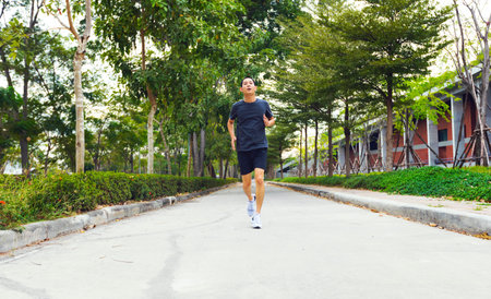 young sporty asian man running at road cover with green tree.