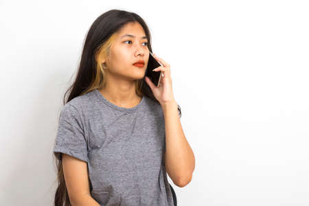 Beautiful young Asian woman smiling sitting relax in the room, using smart phone on white background.の写真素材