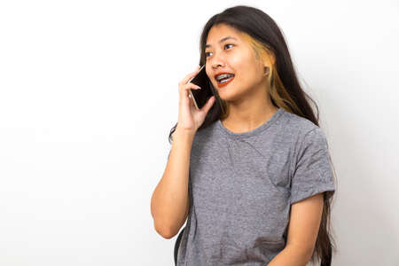 Beautiful young Asian woman smiling sitting relax in the room, using smart phone on white background.の写真素材