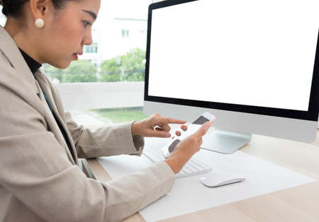 Young beautiful Asian woman using mobile phone and computer, working online at home. Checking smartphone while working.の写真素材