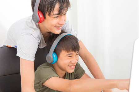 Two multiethnic teenage boys with headphone have fun with computer games at home.の写真素材