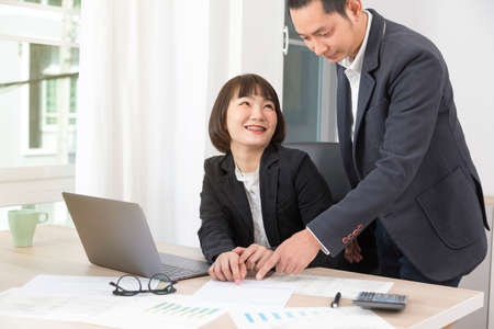 Businesswoman and businessman working together with laptop and graphic charts while sitting at meeting table in modern office.の写真素材