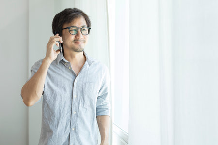 Asian businessman texting on smartphone standing next to window.の写真素材