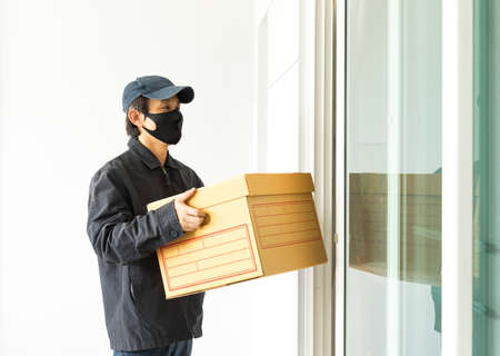 New normal life style. Home delivery shopping box, man wearing gloves and protective mask delivering packages at door.の写真素材
